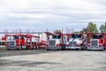 Bright red and white big rigs car haulers semi trucks with empty semi trailers standing on the industrial parking lot waiting for