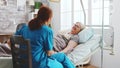 In Bright Retirement Home Old Lady Lying In Hospital Bed Talks With A Female Caregiver
