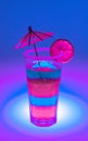 bright rich neon cocktail in a tall glass with an umbrella and a piece of fruit on a neon background