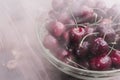 A bright ripe cherry covered with droplets of water lies in a transparent bowl in a cold steam