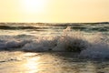 Bright sea sunset. The waves crash into the rock, lit by the warm sunset, sand and pebbles. Sea wave breaks into splashes and whit