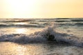 Bright sea sunset. The waves crash into the rock, lit by the warm sunset, sand and pebbles. Sea wave breaks into splashes and whit