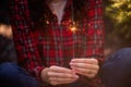 Bright sparkler burns in womans hands. Girl in red checkered shirt smiles. Atmosphere of Christmas Royalty Free Stock Photo