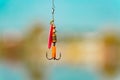 A bright spinner with a triple hook for fishing hangs on a fishing line above the water. Selective focus.