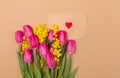 Bright Spring beige background with spring flowers and craft envelope with red heart. Free space. Copy space.Top view Royalty Free Stock Photo