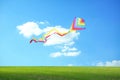 Bright striped rainbow kite flying in blue sky over green grass on sunny day Royalty Free Stock Photo