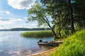 Simple fishers` motorboat, moored to the riparian forest of the lake Seliger under the blinding sunlight, Russia.