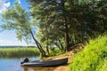 Simple fishers` motorboat, moored to the riparian forest of the lake Seliger under the blinding sunlight, Russia.