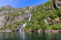 A bright day reveals a waterfall spilling into Trollfjorden\'s clear waters