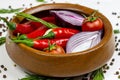 Bright summer vegetables: onion, garlic, tomato, red chili pepper, rosemary in brown wooden bowl and peppercorns on white table