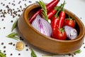 Bright summer vegetables: onion, garlic, tomato, red chili pepper, rosemary in brown wooden bowl and peppercorns on white table Royalty Free Stock Photo