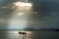 Bright sun rays behind dark clouds shining over people on small boat in the sea