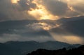 Bright sun rays light shining through dark clouds over mountain at sunset. Dramatic sky in winter Royalty Free Stock Photo