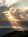 Bright sun rays light shining through dark clouds over mountain at sunset. Dramatic sky in winter Royalty Free Stock Photo