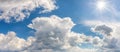 Bright sun shines high in a blue summer sky panorama. Wide shot of spring sky with white clouds on a sunny midday. Weather