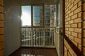 The bright sun shines through the window onto the balcony with bars and plastic windows, on the brick wall.