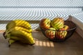 Bright sun shining through window blinds and casting stripes on bananas and aplles in the basket