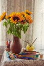 Bright sunflowers in a clay jug on the table by the window. Pencils, paints, and brushes are scattered around Royalty Free Stock Photo