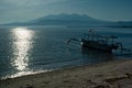 Bright sunny morning on tropical beach, sun glares on water, tradition fishing boat on shore with flag of Indonesia, foggy blue. Royalty Free Stock Photo