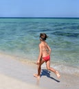 A sunny photo of a little girl in bikini running along a sea shore