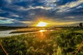 Sunset with lens flare, thick tall grass and bushes with a flat lazy river crossing the horizon Royalty Free Stock Photo