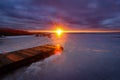 a bright sunset with the sun in a narrow skylight with sunbeams and a dramatic cloudy sky over a frozen lake with an old wooden Royalty Free Stock Photo