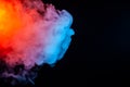 A bright thick cloud of smoke in the shape of a jellyfish hovers backlit with all the colors of the rainbow on a dark background Royalty Free Stock Photo