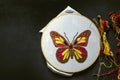 Threads with small scissors and a wooden Hoop with a stretched white cotton fabric and a bright butterfly embroidered on black ply Royalty Free Stock Photo