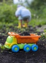 Bright toy dump truck loaded with black soil in the gardens in the spring, in the background a silhouette of a child Royalty Free Stock Photo