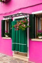 Bright traditional pink house on Burano island, Venice, Italy. Green curtain on door, wooden old style windows with Royalty Free Stock Photo