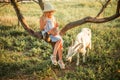 Bright Ukrainian girl with long blond hair in a hat and dress on a farm. Girl 6 years old at sunset sits on a tree and feeds a