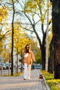 Bright vertical shot of a fashionable woman in casual outfit walking her cute small dog near the beautiful park in the fall season Royalty Free Stock Photo