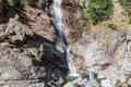 Bright view of flowing Lillaz waterfall with resulted pond beneath and granite karst rocks with evergreen trees, Aosta Valley