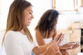 Bright vivid color shot of two young beautiful women sitting on sofa at home using smartphone. Selective focus close up of