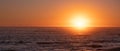 Bright vivid sun on horizon over ocean at sunset, with reflections on water.