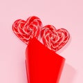 Bright wedding background - couple sweet red lollipops hearts as bouquet on pastel pink, square.