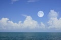 Bright white clouds and the moon in blue sky over green sea Royalty Free Stock Photo