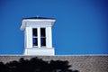 Bright white cupola sits on top of barn roof against a deep blue sky Royalty Free Stock Photo