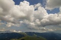 Bright white puffy clouds lit by sun spreading against blue summer sky over green mountain ridge. Royalty Free Stock Photo