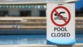 A pool closed sign and pictogram in front of a clean bright blue public outdoor swimming pool