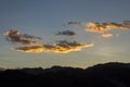 A bright white yellow orange clouds in a sunset dark blue sky over the black silhouettes of the mountains Royalty Free Stock Photo