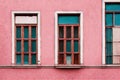 Bright wooden window with crossbars and medieval door on pink wall.