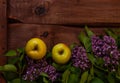 Bright yellow apples, purple lilac flowers with fresh green leaves on wooden background flat lay.Colorful spring summer Royalty Free Stock Photo