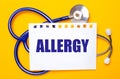 On a bright yellow background, a blue stethoscope and a sheet of paper with the text ALLERGY. Medical concept