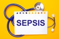 On a bright yellow background, a blue stethoscope and a sheet of paper with the text SEPSIS. Medical concept