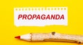 On a bright yellow background, a large wooden pencil and a sheet of torn paper with the text PROPAGANDA Royalty Free Stock Photo