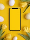 Bright yellow background with smartphone surrounded by easter eggs and tulips. Minimalist spring design Royalty Free Stock Photo