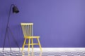 Bright, yellow chair standing next to a black lamp against purple wall in simple room interior. Real photo Royalty Free Stock Photo