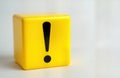 Bright yellow cube with black exclamation mark symbol. Simple design conveys urgency. Isolated on white background. Suitable for