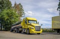 Bright yellow day cab big rig semi truck with shiny tank semi trailer standing on the rest area parking lot with trees along Royalty Free Stock Photo